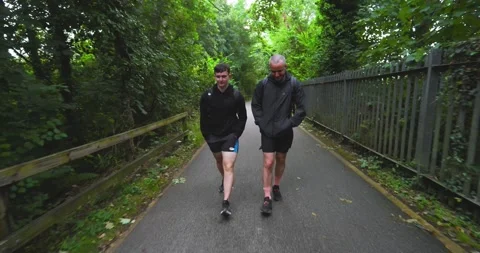 Two men walking on forest path wearing athletic gear, enjoying outdoor exercise Stock Footage 345886072