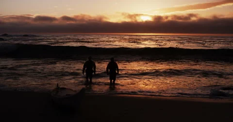 Two Men Walking Out Of Stormy Ocean During Fiery Sunset In Slow Motion Wide Shot Stock Footage 64317499