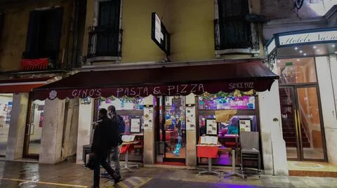 Two men walking passing by dining restaurant on street of Venice. Stock Photos