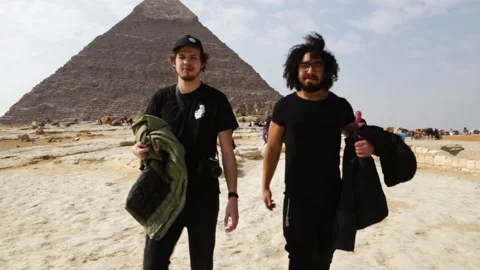 Two Men Walking with Pyramids in Background Stock Footage 146051047