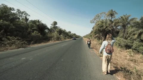 Two men walking on rural Casamance road at midday, one white tourist  Stock Footage 309989920