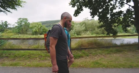 Two men walking on scenic path with backpacks, enjoying outdoor exercise on a Stock Footage 345715486