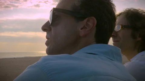 Two men watching something on the beach overlooking a sunset Stock Footage 55414656
