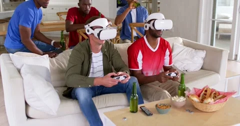Two men wearing white VR headsets are playing controllers on couch while game is Stock Footage 335366026