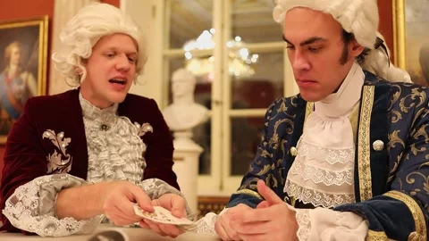 Two men in wigs and historical suits play cards Stock Footage 299628571