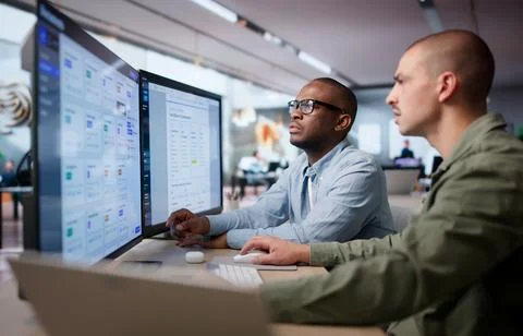 Two Men Work Together Managing Secure Digital Documents On Desktop Computers. Foto stock