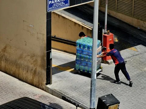Two men in work uniforms are pushing a large cart stacked high with Stock-Fotos