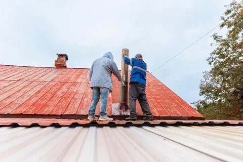 Two men worker installing metal chimney on red house roof. Professional Fotos de archivo