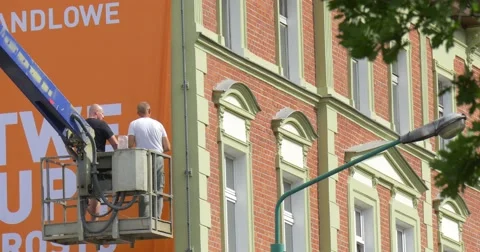 Two Men Workers in Truck Tower are Installing an Orange Advertisement Banner Stock Footage 54839346