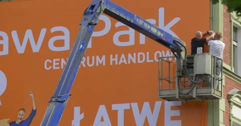 Two Men Workers in a Truck Tower Are Installing an Orange Advertisement Banner Stock Footage 54850112