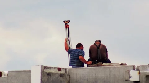 Two men working on construction site, one holding surveying equipment, Stockbeeldmateriaal 325298265