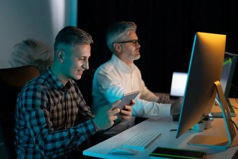 Two Men Working Late On Computers And Digital Devices Stock Photos