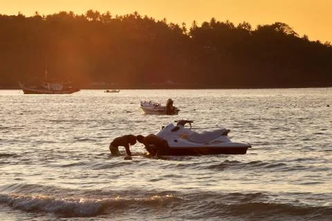 Two mens at sunset pull hydrocycle out of the water. Summer vacation. Water b 스톡 사진