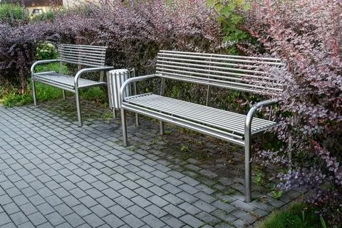 Two metal benches by a pathway surrounded by flowering shrubs in a park during Stock Photos