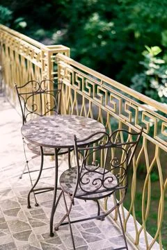 Two metal chairs with openwork backs stand near a round table on the terrace Stock Photos