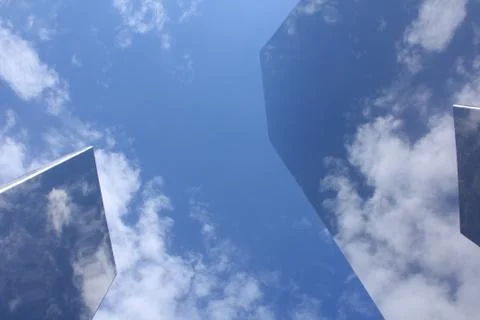 Two metal objects reflecting a blue sky with white clouds. Stock Photos