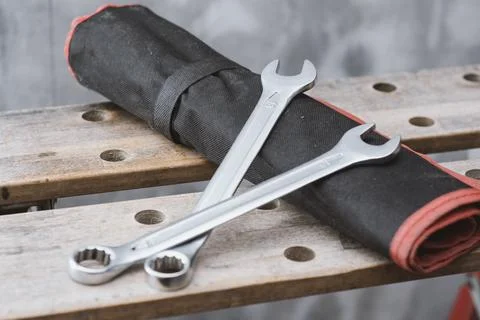 Two metal wrenches on a red tool bag lying on a perforated wooden workbench.. Stock Photos