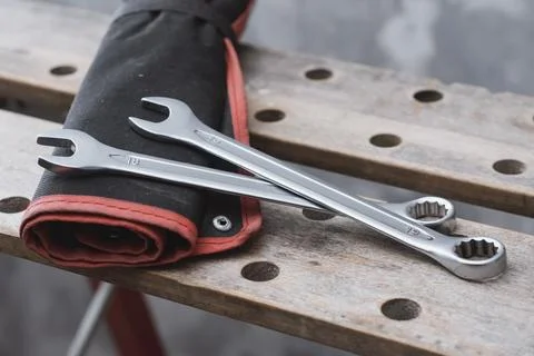 Two metal wrenches on a red tool bag lying on a perforated wooden workbench.. Stock Photos