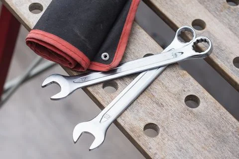 Two metal wrenches on a red tool bag lying on a perforated wooden workbench.. Stock Photos