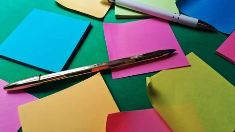 Two metallic pens resting on vibrant colorful sticky note papers Stock Photos