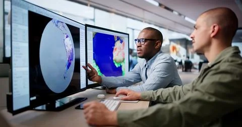 Two Meteorologists Use Computers In Office Analyzing Hurricane Risk Data. Stock Photos