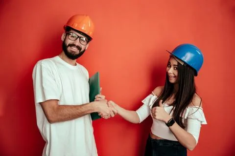 Two mid adults constructors workers giving hand shake isolated on red background Stock Photos
