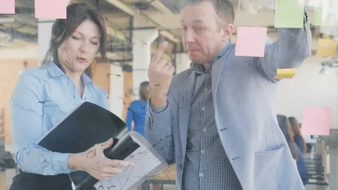 Two middle-aged developers, a man and a woman, write formulas on a glass board Stock Footage 108983467