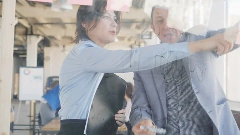 Two middle-aged engineers, a man and a woman, write formulas on a glass board Stock Footage 108983144