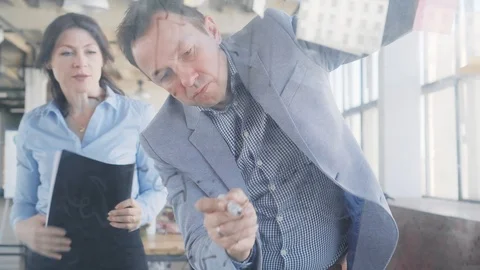 Two middle-aged managers, a man and a woman, write formulas on a glass board Stock Footage 108982648