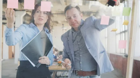 Two middle-aged managers, a man and a woman, draws graphics on a glass board Stock Footage 108983682