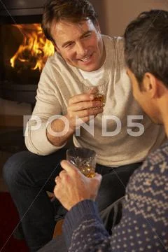 Two Middle Aged Men Relaxing Sitting On Sofa Drinking Whisky Stock Photos
