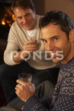 Two Middle Aged Men Relaxing Sitting On Sofa Drinking Whisky Stock Photos