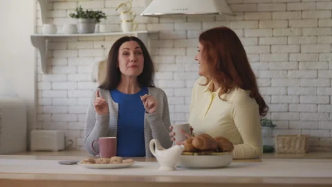 Two middle-aged sisters gossiping and laughing in the kitchen, family bonding Stock Footage 337947526