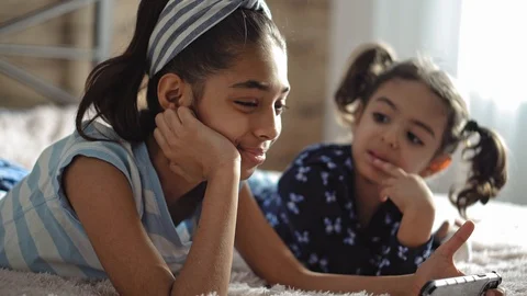 Two middle eastern young girls on the bed with a smartphone. Two dark-skinned Stock Footage 125053157