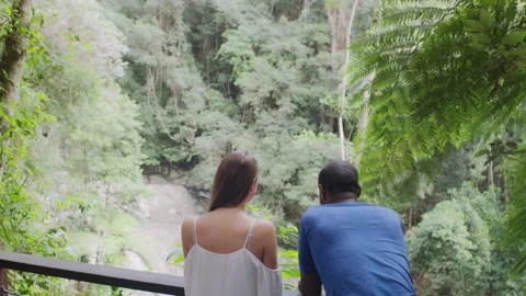 Two millennial friends leaning on railing in front of small waterfall in an Aust Stock Footage 199459400