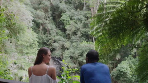 Two millennial friends leaning on railing in front of small waterfall in an Aust Stock Footage 199460544