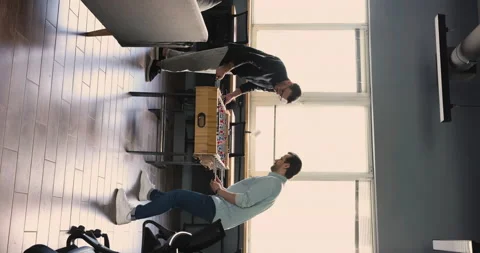 Two millennial men engaged in table soccer game in workspace Stock Footage 221670064