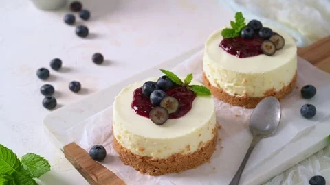 Two mini cheesecakes with berry compote and fresh mint on a white textured surfa Stock Footage 341366019