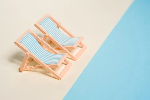 Two miniature deck chairs on yellow and blue background representing sand a.. Stock Photos