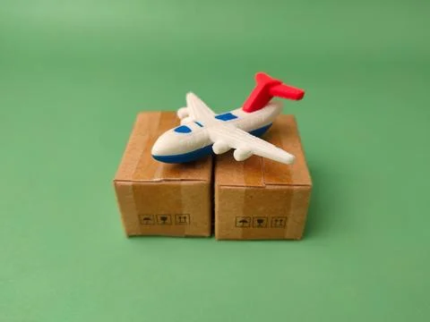 Two miniature shipping boxes, one topped with a toy airplane on green backg.. Stock Photos