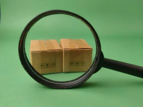 Two miniature shipping boxes viewed through the lens of a black magnifying .. Stock Photos