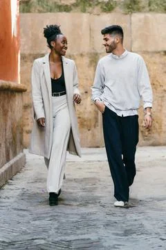 Two models of different ethnicities walking while chatting outdoors Stock Photos