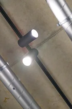 Two modern ceiling lights mounted on a concrete ceiling with exposed metal pi Stock Photos