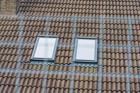 Two modern skylight windows installed on a tiled roof with brick wall section Stock Photos