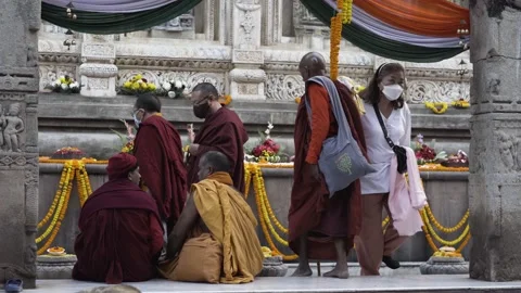 Two monks seating and talking, people walking around Mahabodhi temple complex. Stock Footage 230161170