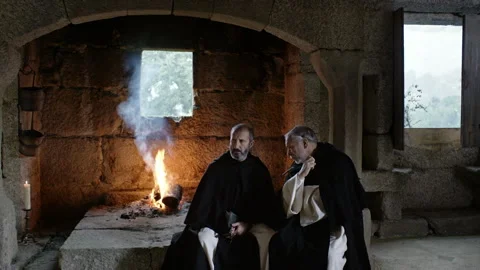 Two monks share a quiet conversation by the fire in a stone building Stock Footage 327950941