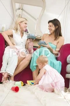 Two mothers in living room with babies and coffee smiling Stock Photos