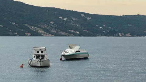Two motorboats float on calm Kotor Bay water in Montenegro with a mountain coast Stock Footage 344902789
