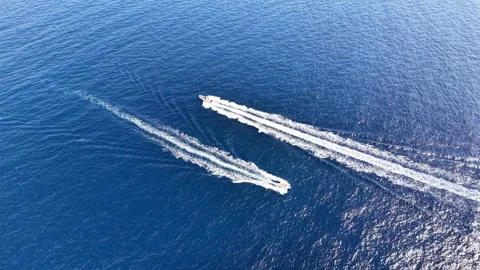 Two motorboats navigate across a vast blue ocean leaving distinct wake trails Stock Footage 345149563