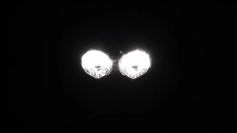 Two motorcycle headlights turning on and illuminating on black background Vídeo Stock 145487591